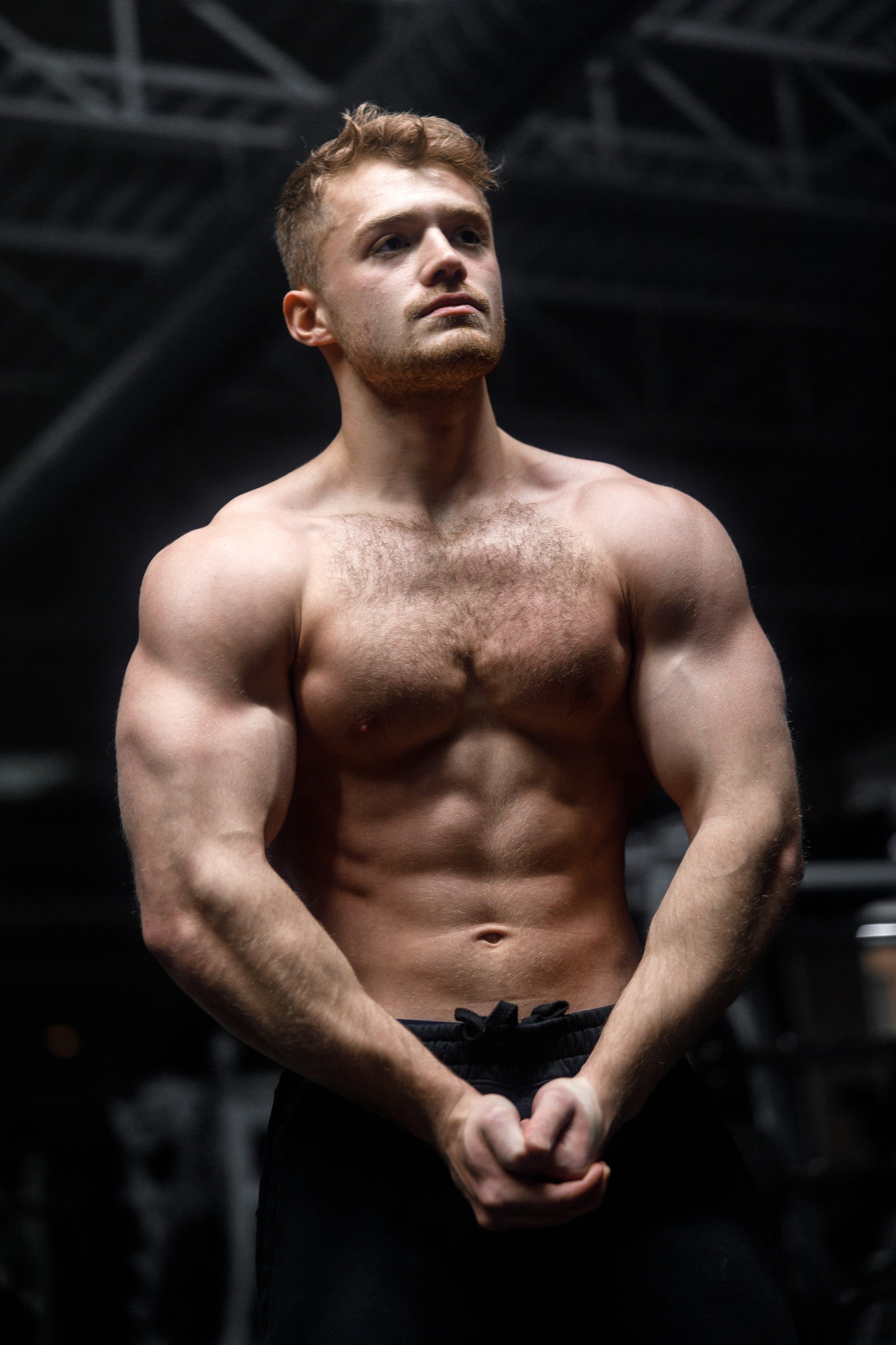 Low-key physique portrait sculpted by overhead gym lighting